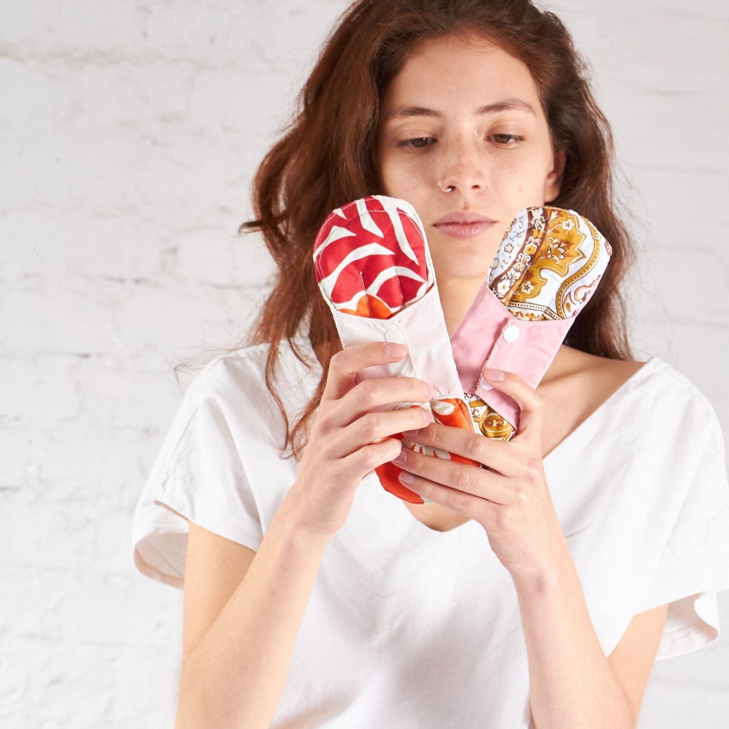 una mujer con dos Toallas higiénicas reusable en tela en su manos.