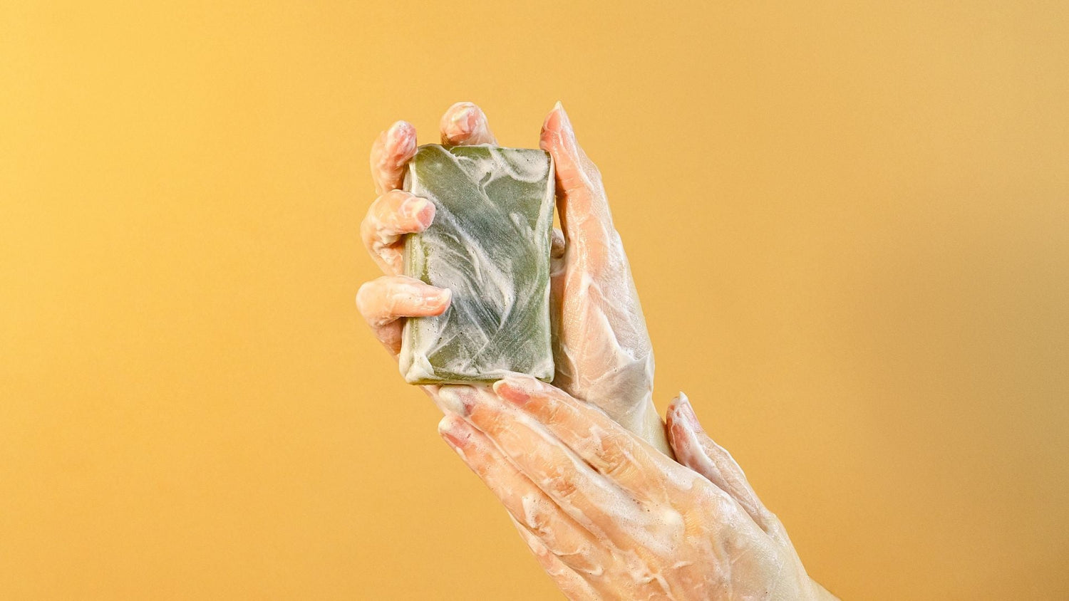 un jabon artesanal en los manos de una mujer con fondo plano color amarillo. 