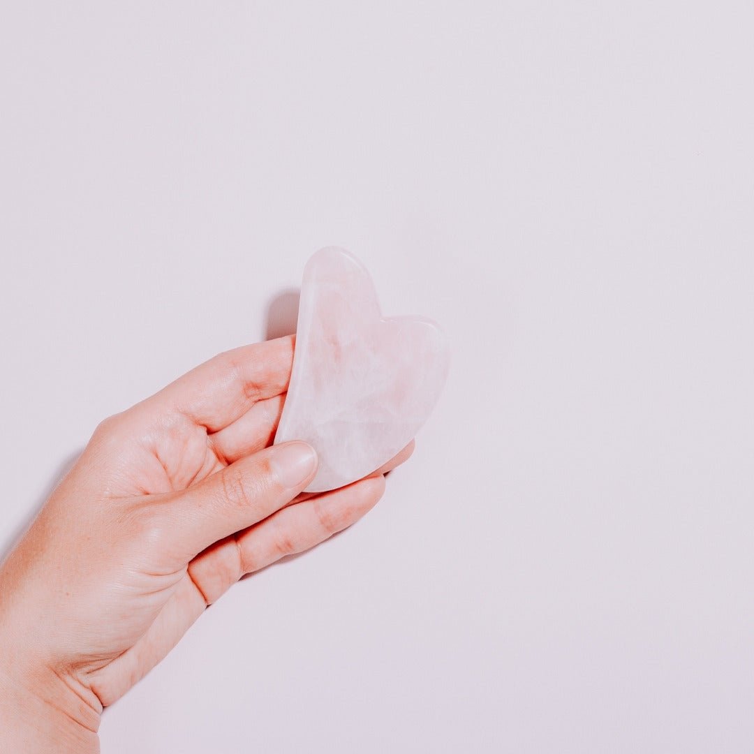 Gua Sha Cuarzo Rosa en un mano de una mujer con fondo blanco 